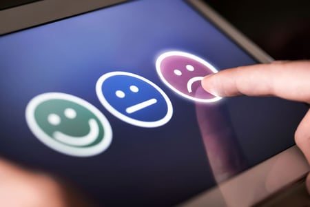 Person drückt auf traurigen Smiley symbolisierend für Beschwerdemanagement