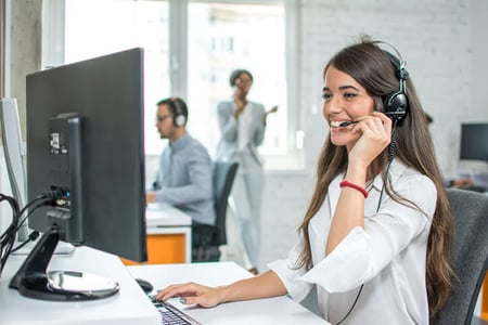 Frau mit Headset sitzt vor einem Computer und telefoniert