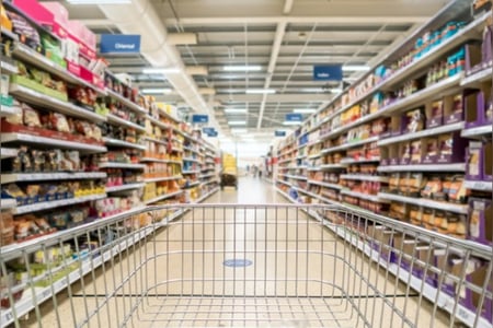Ein Einkaufswagen fährt an den Supermarktregalen mit Hersteller- und Handelsmarken vorbei