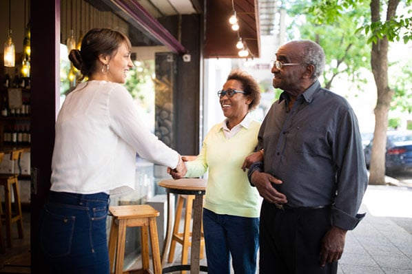 Frau schüttelt älterem Ehepaar die Hand vor Café als Symbol für gutes Kundenerlebnis