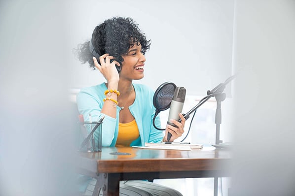 Frau nimmt Marketing-Podcast mit Mikrofon und Kopfhörern auf