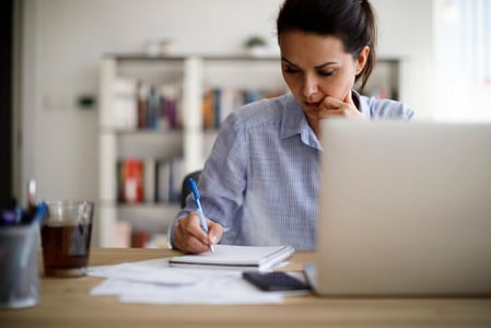 Frau sitzt am Schreibtisch und erstellt Projektbeschreibung mit Laptop und Schreibblock