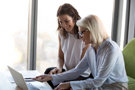 Zwei Frauen sitzen vor Laptop und besprechen etwas