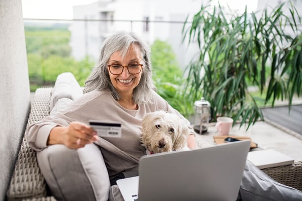 Frau sitzt mit Hund auf Sofa und betreibt Online-Shopping
