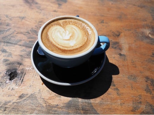 Tasse Cappuccino auf Holztisch bei Sonnenschein
