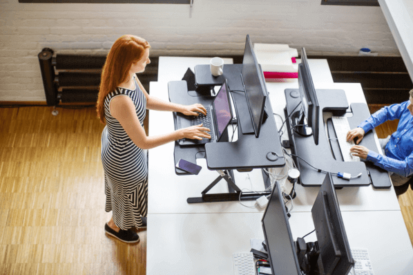 Frau arbeitet am Stehtisch im Büro für mehr Bewegung am Arbeitsplatz