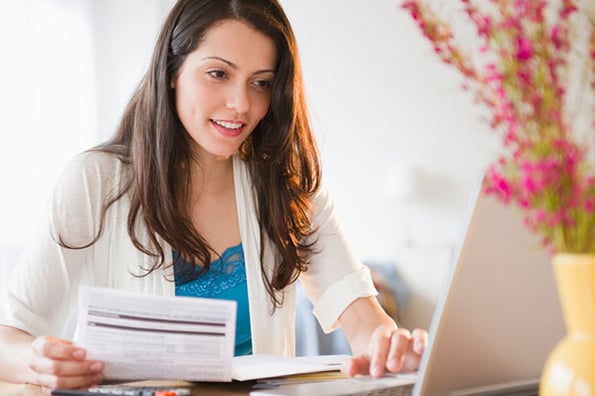Frau am Laptop mit Rechnungen in Hand arbeitet entsprechend Buchführungspflicht