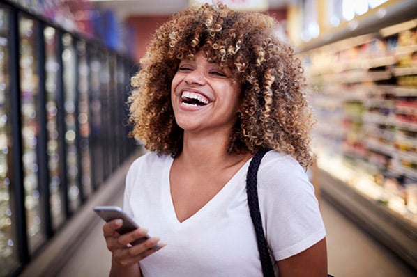 Lachende Kundin mit Smartphone im Geschäft steht für Customer Obsession