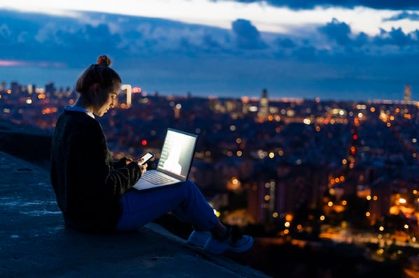 Frau am Plattformrand über Stadt mit Laptop symbolisierend für Edge Computing