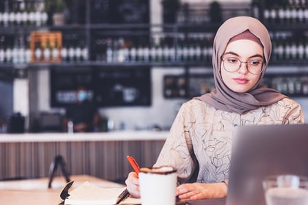 Frau im Café arbeitet am Laptop und schreibt Notizen runter zu Helpful Content Update