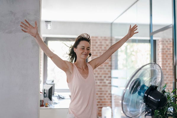 Frau steht vor Ventilator wegen Hitze im Büro