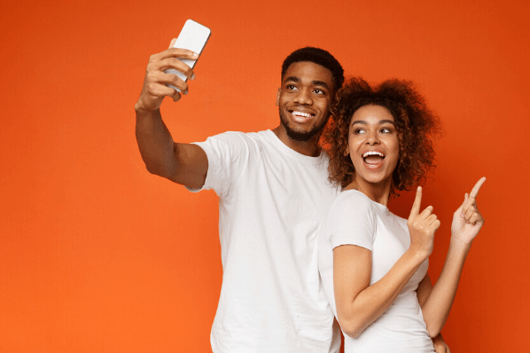 Mann und Frau erstellen Instagram Reel mit Smartphone vor orangenem Hintergrund