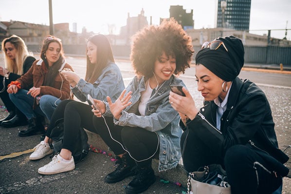 Frauen sitzen draußen auf Bordstein und erstellen Instagram-Gruppe
