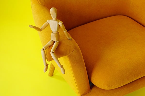 Mannequin aus Holz sitzt auf orangenem Stuhl symbolisierend für Körpersprache deuten
