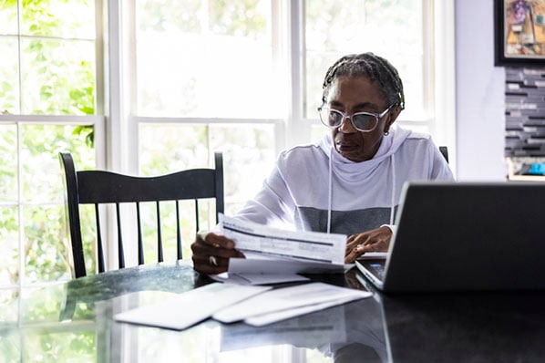 Frau mit Rechnungen am Laptop führt Kosten- und Leistungsrechnung durch
