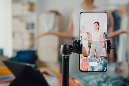 Frau auf Smartphone-Screen beim Live-Shopping von Kleidung