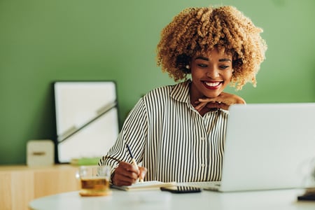 Frau am Laptop notiert Ideen zu Newsletter-Texten auf Papier