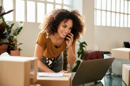 Frau, umgeben von Boxen, telefoniert beim Erstellen eines Onlineshops