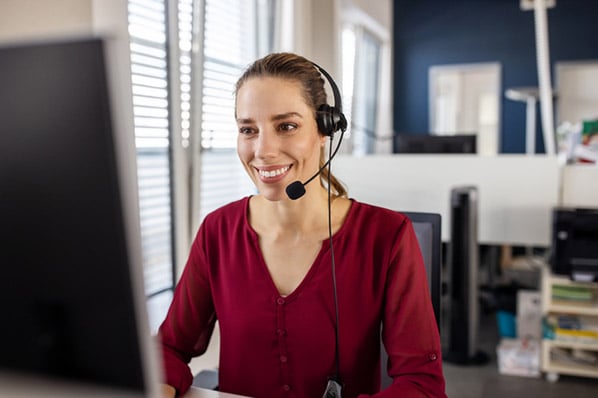 Mitarbeiterin mit Headset am Monitor lächelt dank Outsourcing