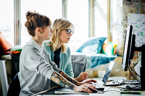 Zwei konzentrierte Frauen vor Monitor üben PowerPoint-Shortcuts