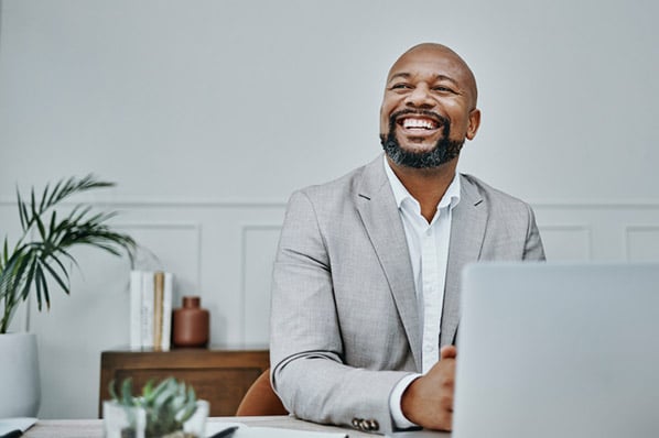 Lächelnder Produktmanager vor Laptop in grauem Anzug schaut zur Seite