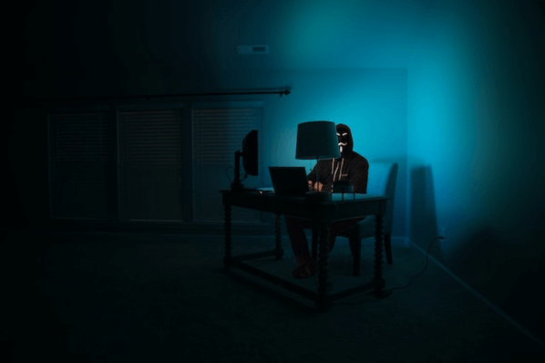 Maskierte Person am Rechner betreibt Social Engineering