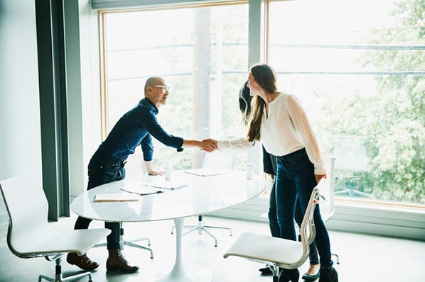 Frau schüttelt Hände mit Mann beim Meeting zu B2B-Vertrieb im Büro
