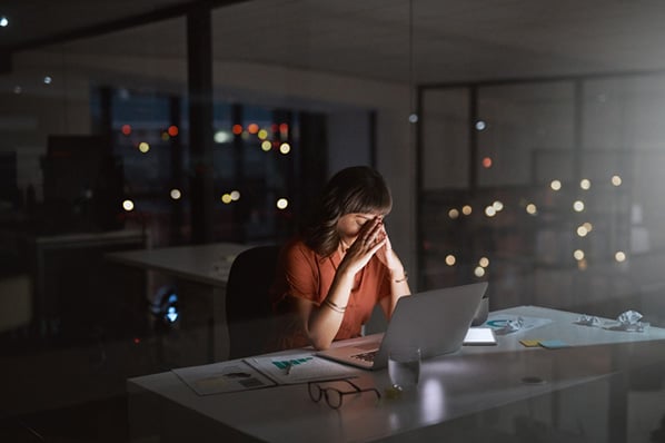 Frau nachts im Büro vor Laptop erlebt Überforderung im Job