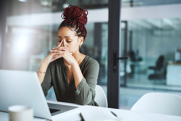 Frau vor Laptop fast sich an Stirn, weil sie unzufrieden im Job ist