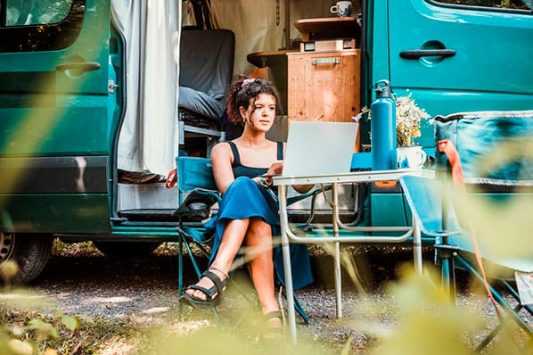 Frau in Campingstuhl vor Campingwagen informiert sich über Urlaubsanspruch am Laptop