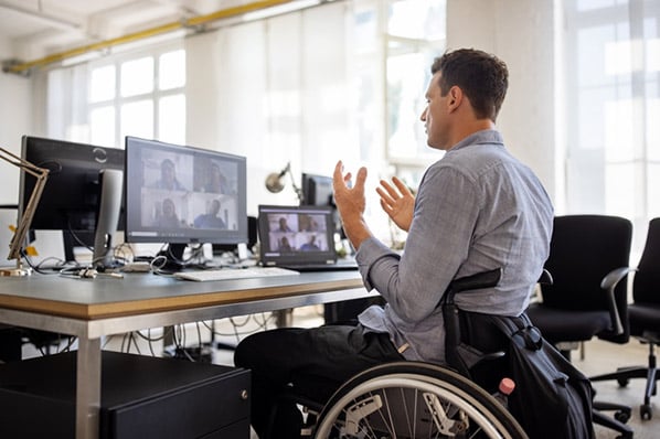 Mann in Rollstuhl gestikuliert vor Monitor mit Webinar-Landingpage