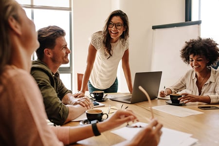 Frau am Laptop am Tisch spricht mit Ihrem Team ueber Wissenstransfer im Unternehmen