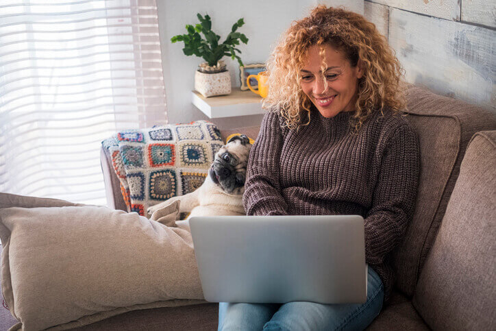 Frau sitzt mit Hund auf dem Sofa und erstellt einen Blog mit einem Laptop