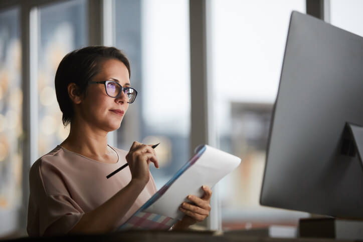 Frau hält Stift und Notziblock in den Händen und betrachtet Computer Bildschirm