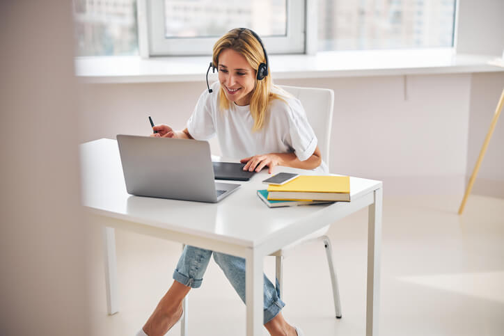 Frau mit Headset sitzt an einem Schreibtisch und arbeitet an einem Laptop