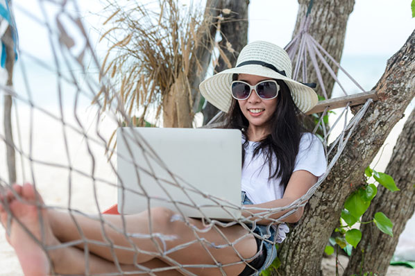 Digitale Nomadin arbeitet mit Laptop in Hängematte am Strand
