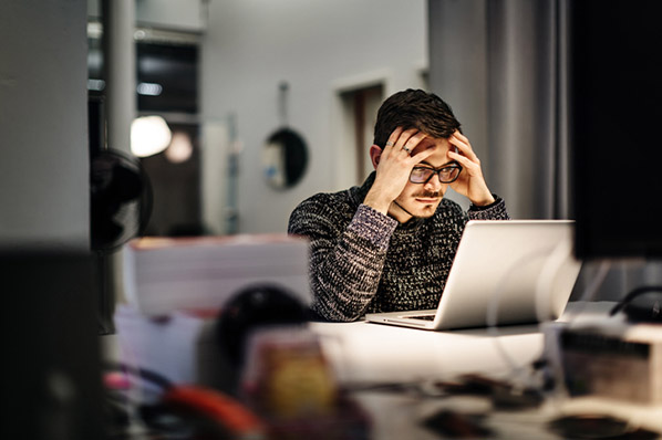 Mann im dunklen Büro vor ausgeleuchtetem Laptop arbeitet verzweifelt an Disaster Recovery