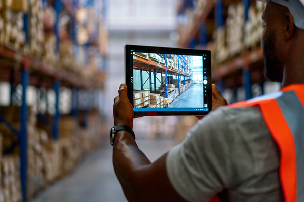 Arbeiter in Lagerhalle mit Tablet dokumentiert Distributionsgrad