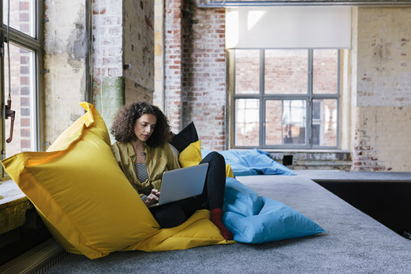 Mitarbeiterin sitzt auf gelbem Sitzsack und erstellt Google-Konto auf Laptop