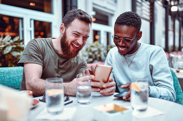 Maenner am Esstisch lachen beim Instagram-Umfrage erstellen auf Smartphone