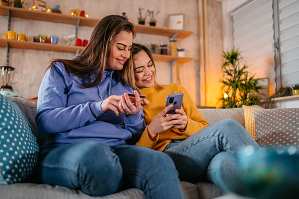 Frauenpaar auf Sofa nutzt Pinterest Shopping auf Smartphone