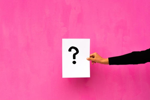 Als Symbol für Quiz erstellen: Eine Hand die ein Blatt mit Fragezeichen auf einem pinken Hintergrund hält