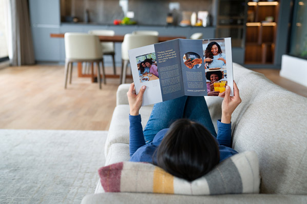 Liegende Frau auf Sofa liest Magazin mit Schleichwerbung