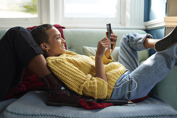 Junge Frau liegend auf Sofa mit Smartphone shoppt über Social Commerce