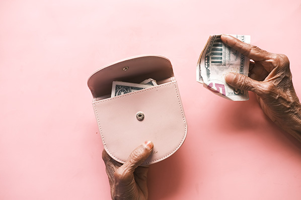 Hand hält Geld und kleine Tasche auf rosa Hintergrund symbolisierend für variable Vergütung
