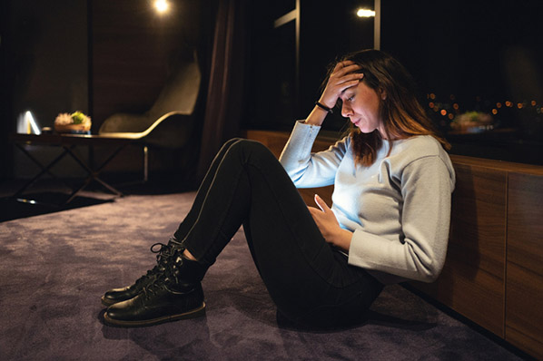 Frau in dunklem Zimmer verzweifelt vor Smartphone wegen XSS-Angriff 